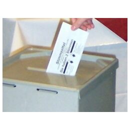 Foto einer Wahlurne, in die ein Stimmzettel geworfen wird.